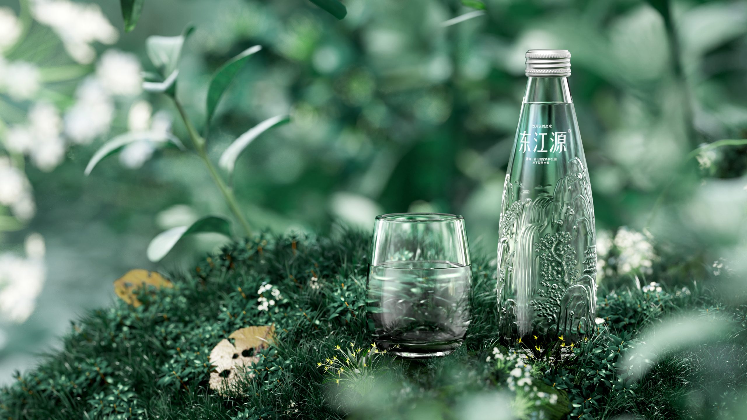 A clear glass bottle of water with intricate designs, placed next to a glass filled with water, surrounded by green foliage and small flowers.